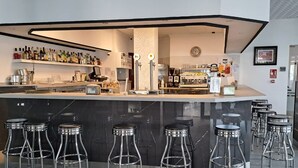 A modern bar area with a central island, bar stools, and a variety of bottles and glasses on shelves. - Hotel Costamar (Torrox)
