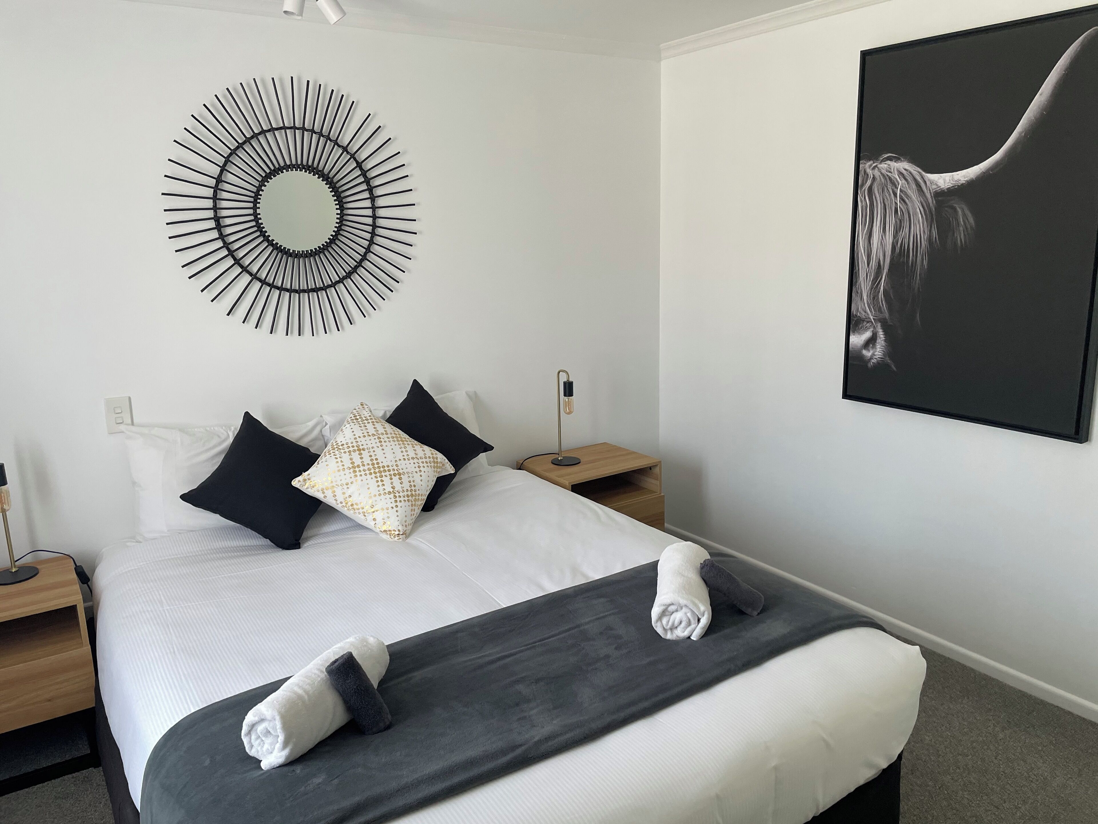 Una cama impecablemente arreglada con ropa de cama blanca y negra, un cuadro abstracto en blanco y negro, y una decoración de pared moderna.