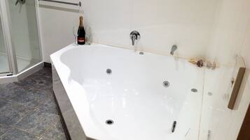 Eine große weiße Badewanne mit mehreren Wasserhähnen, eine Champagnerflasche und zwei leere Gläser.