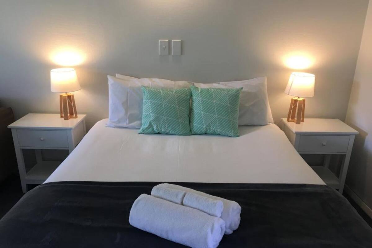 A neatly made bed with white and green pillows, two bedside lamps, and a black bedspread.