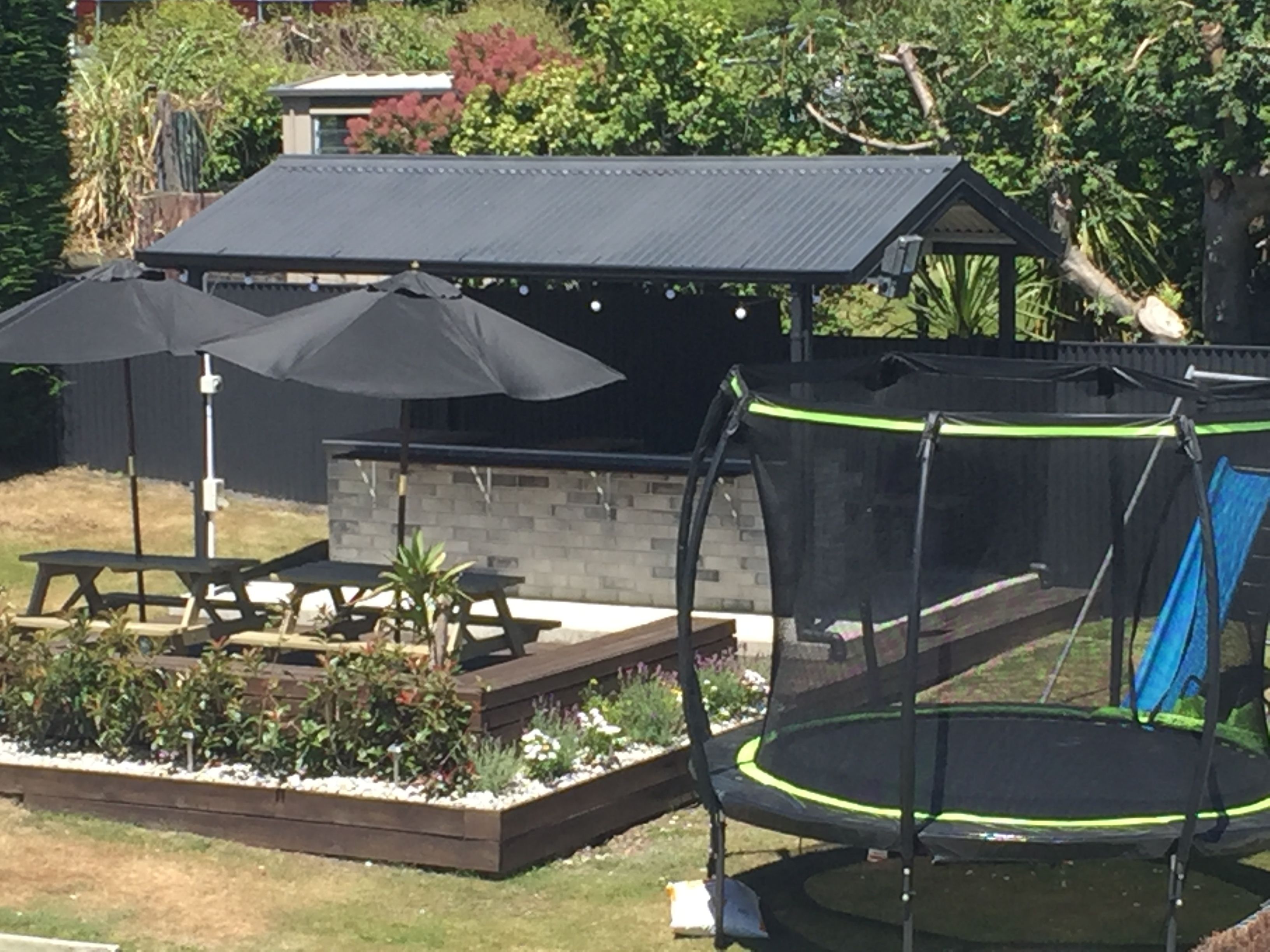 A backyard with a trampoline, picnic table, and umbrellas.