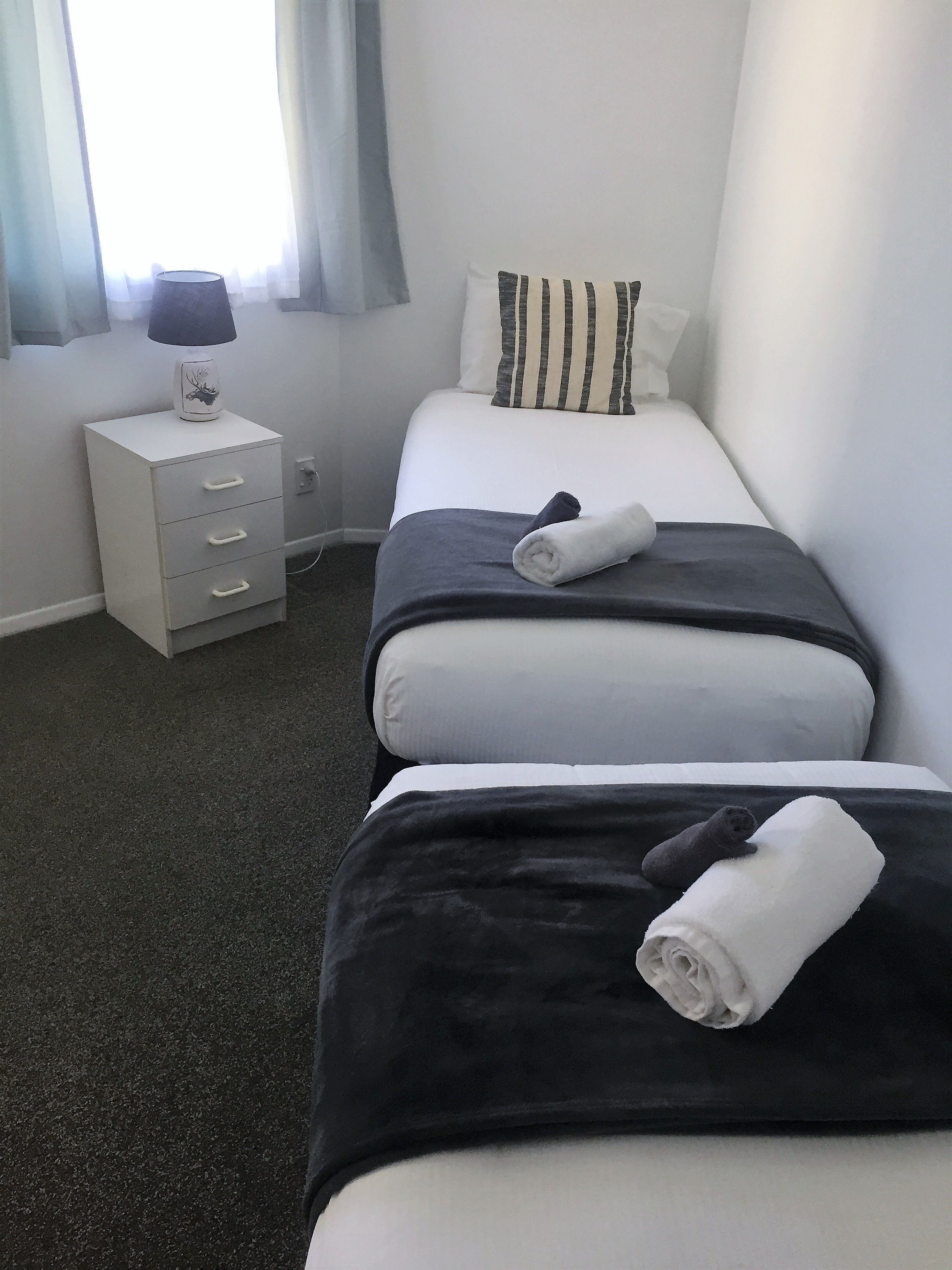 A hotel room with two beds, a bedside table with a lamp, and a window with curtains.