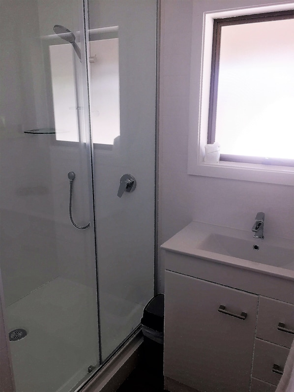 A bathroom with a glass shower enclosure, a sink, and a window. - Fairway Motel and Apartments (Wanaka)