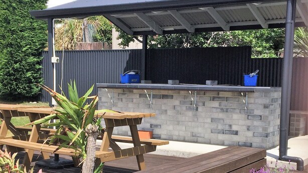 An outdoor patio area with wooden benches, a stone wall, and a covered seating area. - Fairway Motel and Apartments (Wanaka)