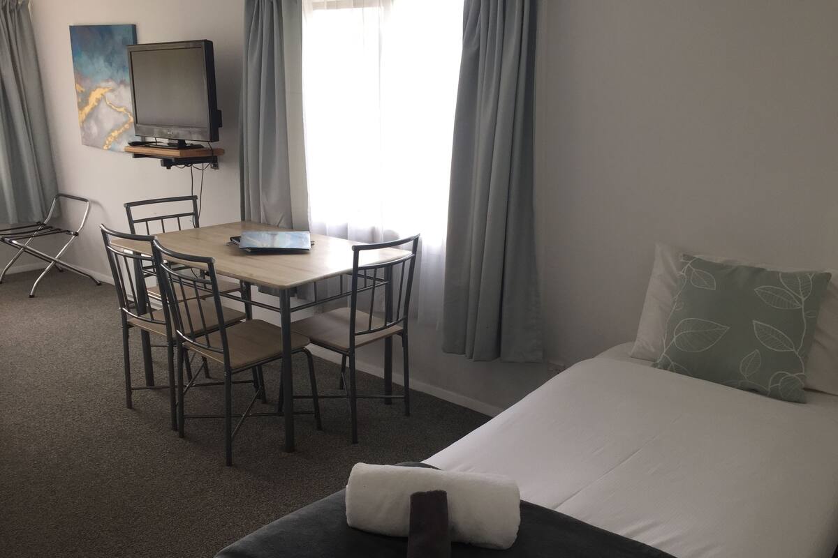 A hotel room with a bed, a desk with a laptop, a chair, and a TV.