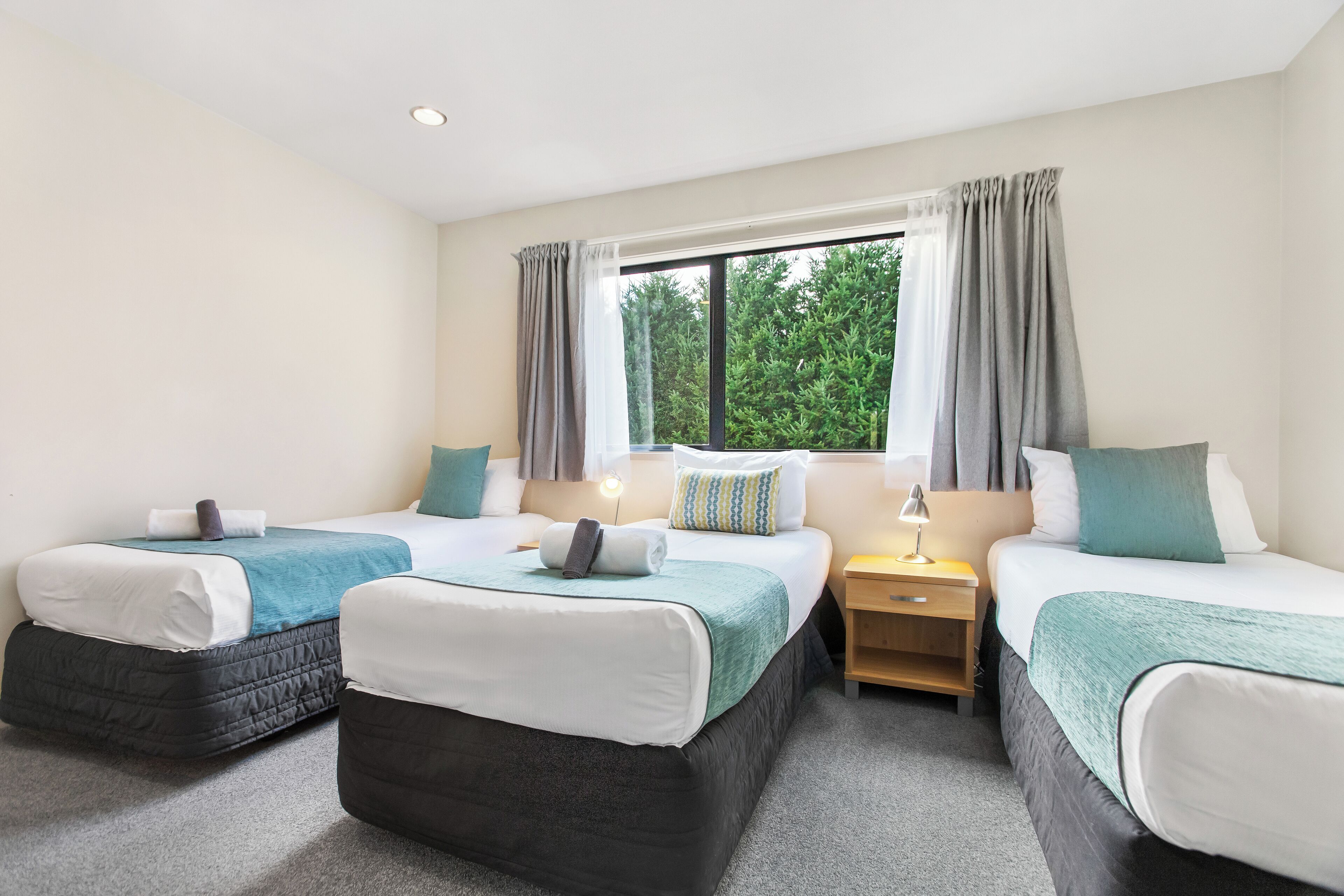 A hotel room with two single beds, a nightstand with a lamp, and a window with curtains.