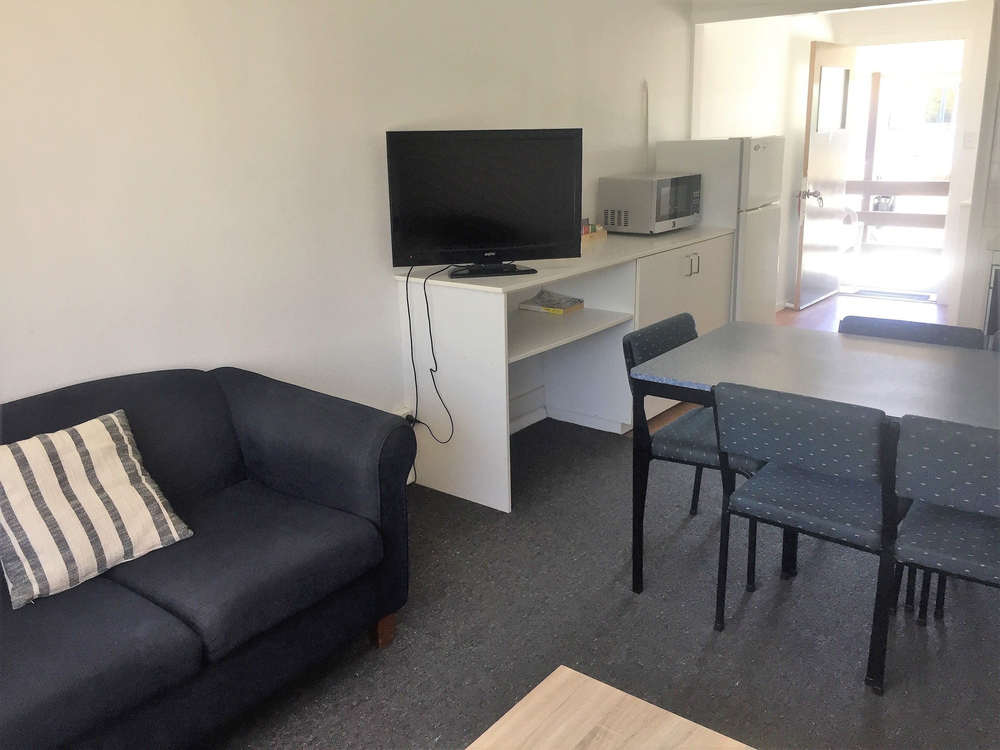 A compact living space with a sofa, a TV, a dining table, and a microwave.