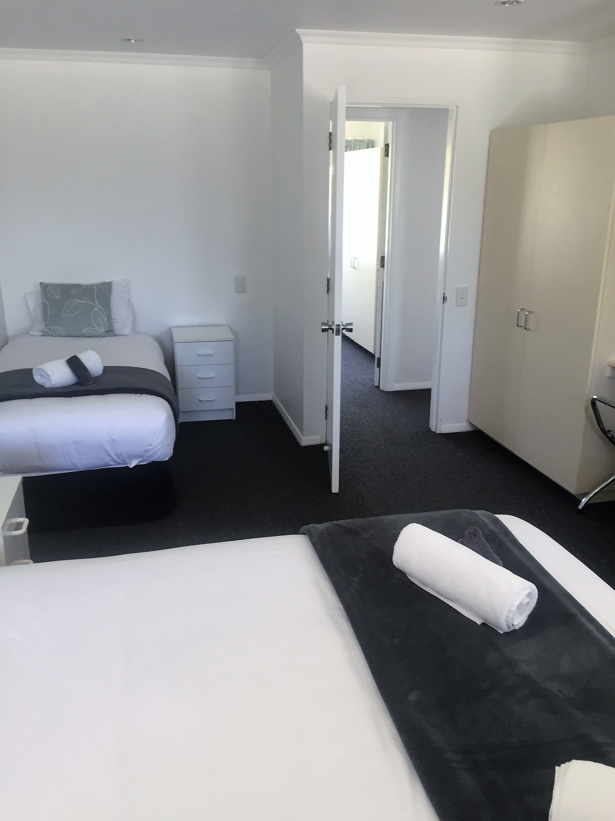 Una habitación de hotel con cama, mesita de noche, armario y una puerta abierta que da a otra estancia.