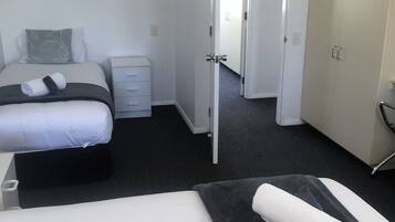 Una habitación de hotel con cama, mesita de noche, armario y una puerta abierta que da a otra estancia.