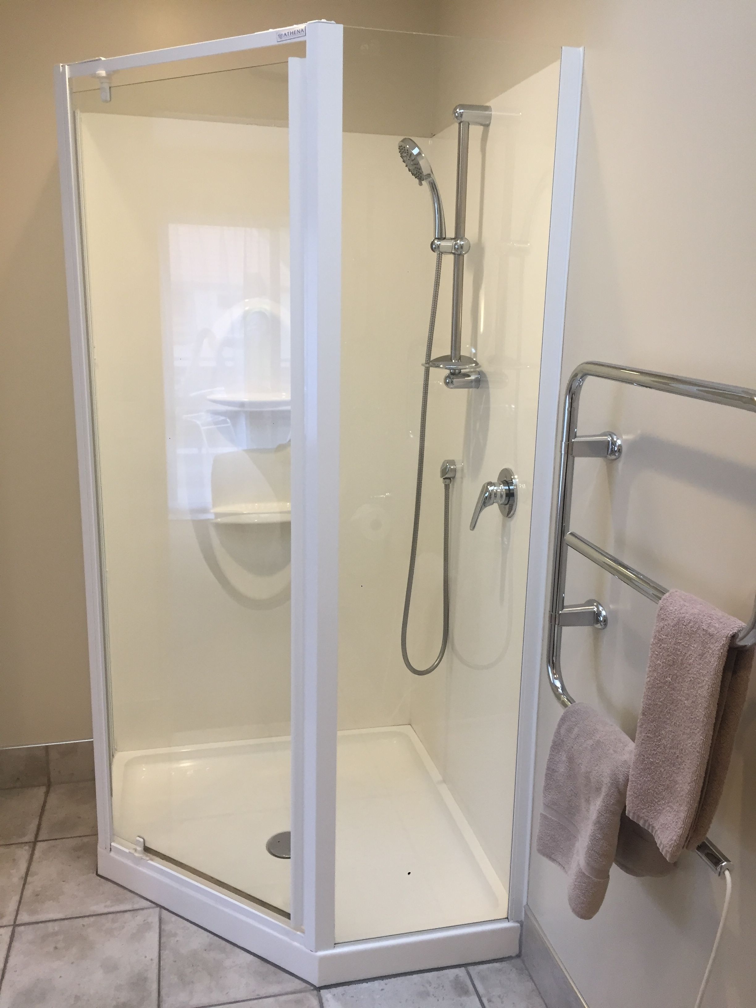 Un espace douche fermé par des parois de verre, avec une porte blanche, un porte-serviettes muni d’une serviette et un pommeau de douche.