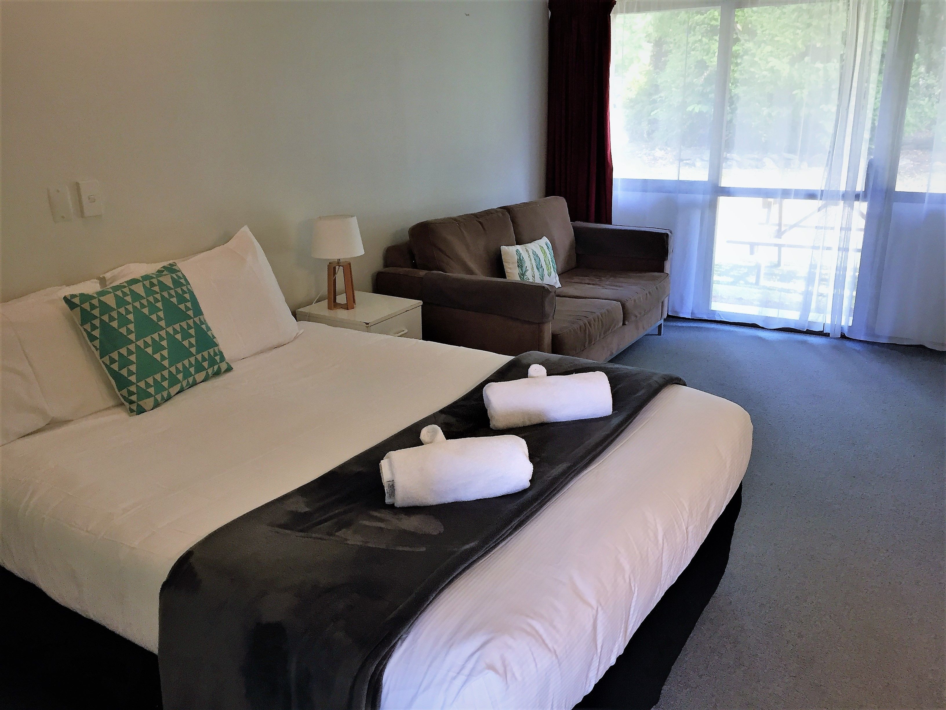 A hotel room with a bed, a sofa, a nightstand, and a window with curtains.