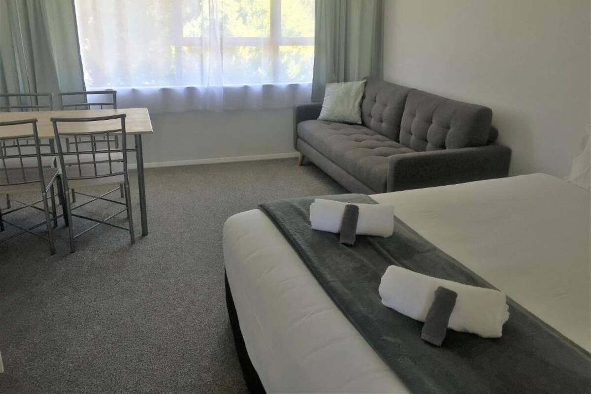 A hotel room with a bed, a sofa, a dining table with chairs, and a window with curtains.