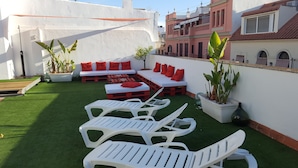 A rooftop patio with white lounge chairs, red cushions, and potted plants. - Hotel y Apartamentos Doña Lola (Seville)