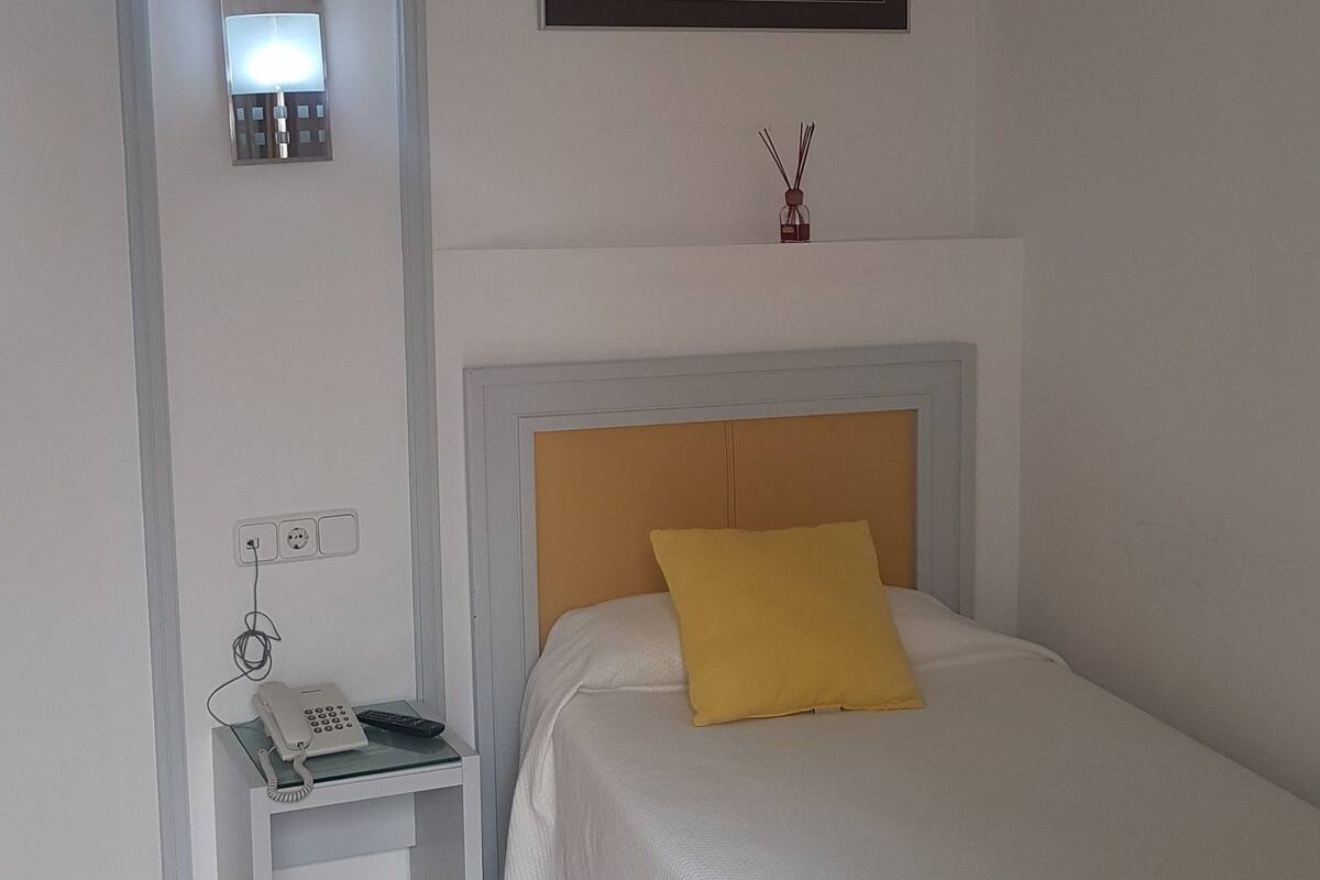 A bedroom with a bed, bedside table, and a wall-mounted light.