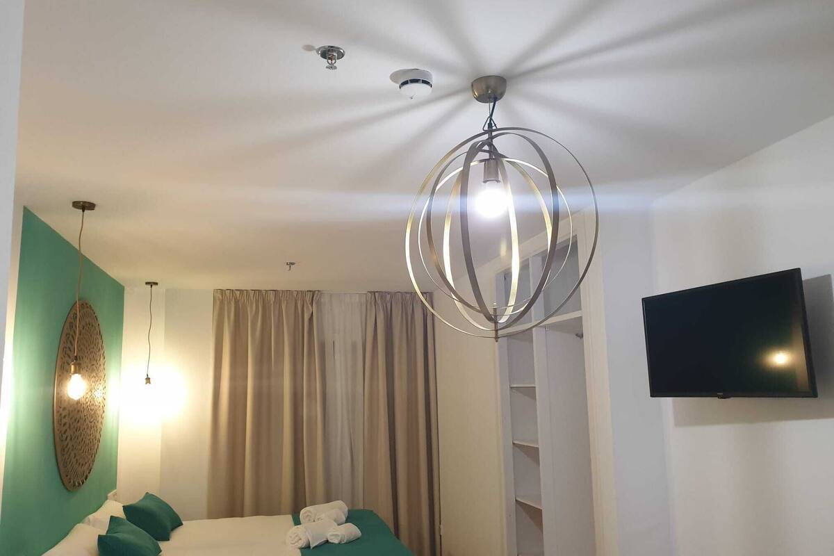 A hotel room with a bed, a television, a chandelier, and a wall-mounted TV.