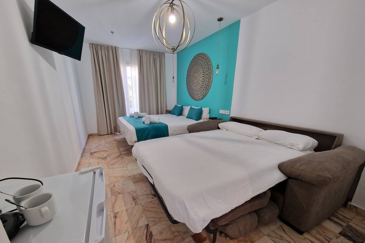 A hotel room with two beds, a sofa, a flat-screen TV, a decorative wall piece, and a marble floor.