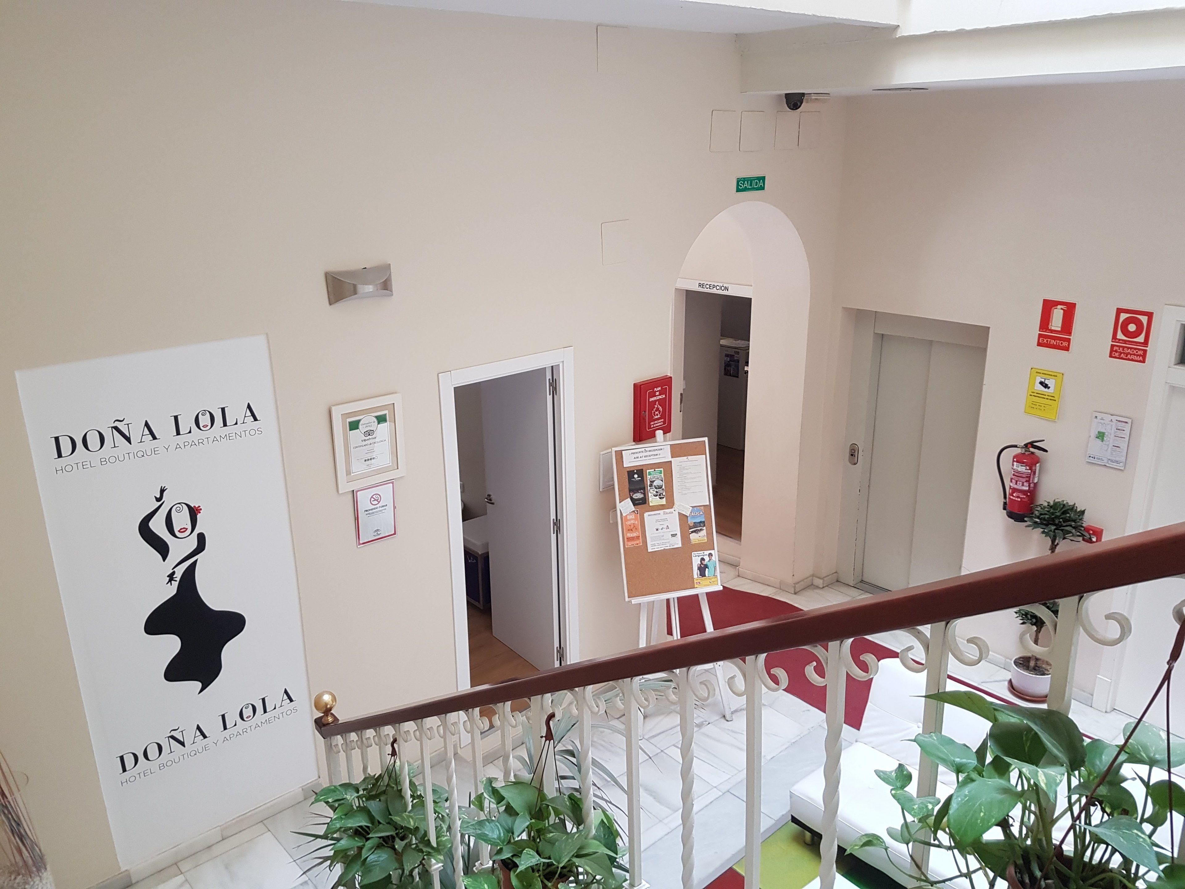 A hotel interior with a reception desk, a bulletin board, and a staircase with railings.