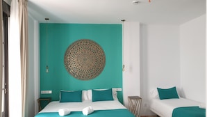 A hotel room with a bed, a smaller bed, teal and white bedding, a decorative wall hanging, and a small side table. - Hotel y Apartamentos Doña Lola (Seville)