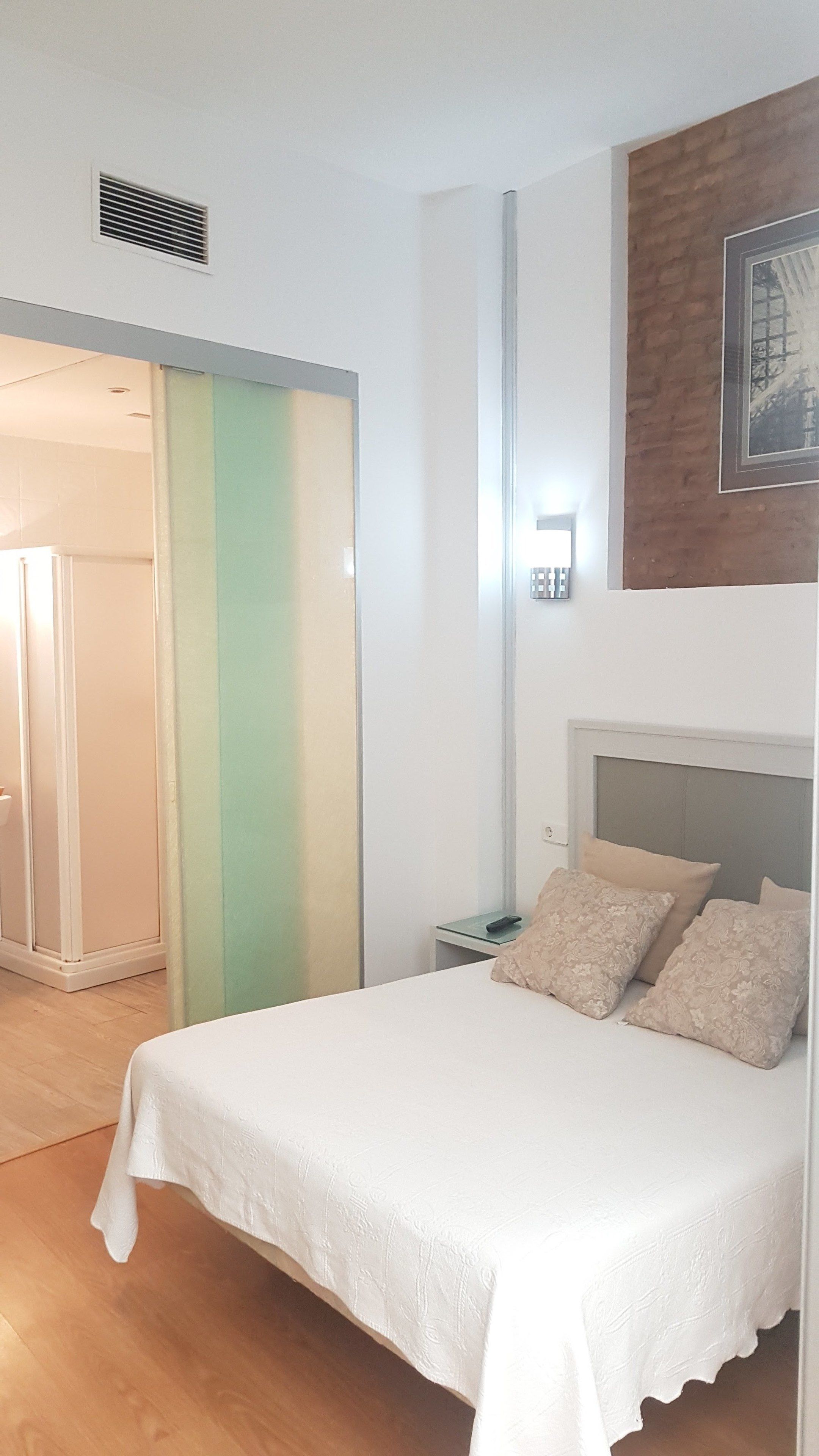 A bedroom with a bed, pillows, a nightstand, a wall-mounted light, and a door leading to a bathroom.