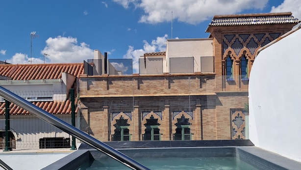 A swimming pool with a metal railing, a clear blue sky, and a building with traditional architecture in the background. - Hotel y Apartamentos Doña Lola (Seville)