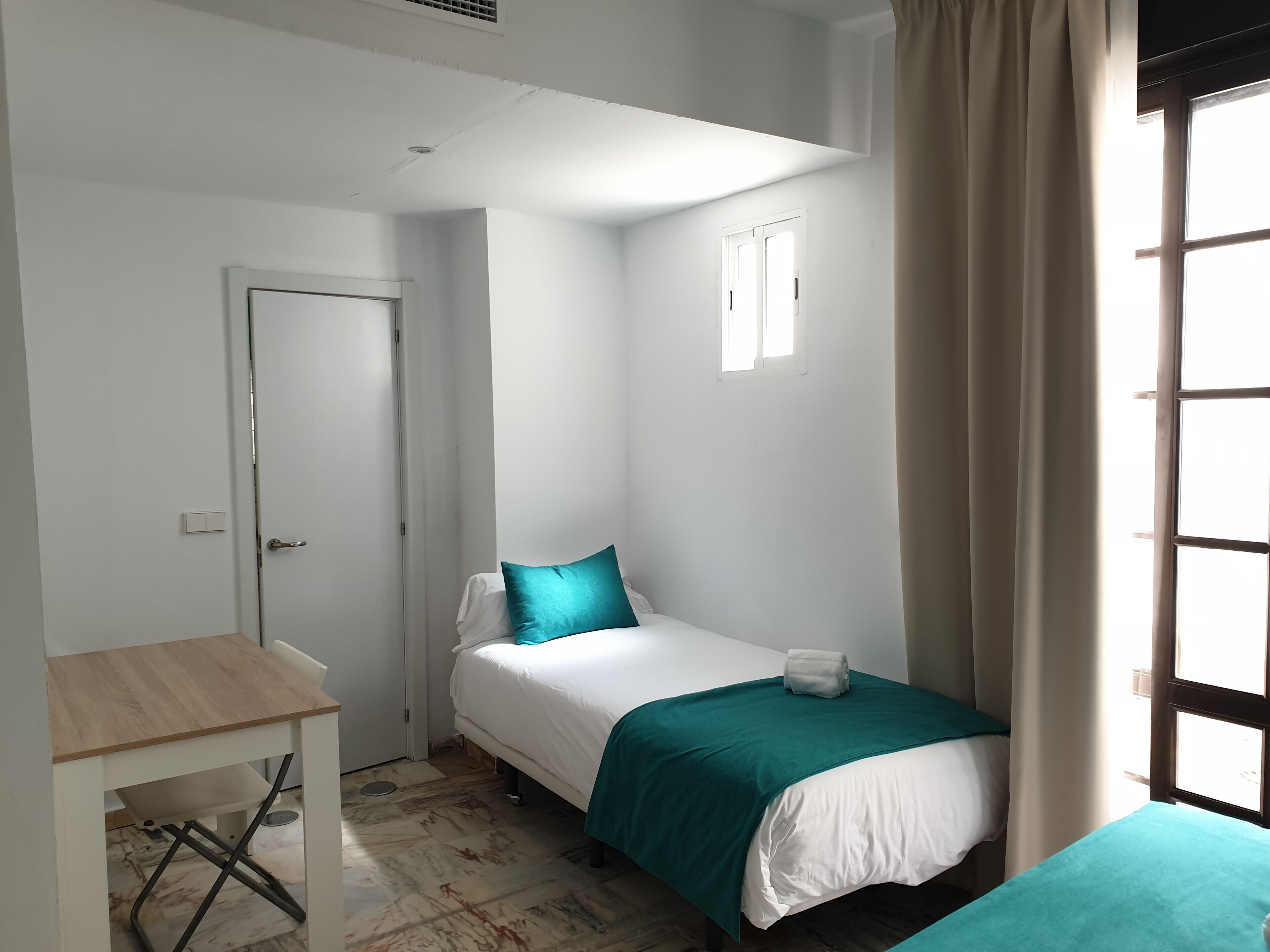 Una habitación pequeña y limpia con cama, mesa y ventana.