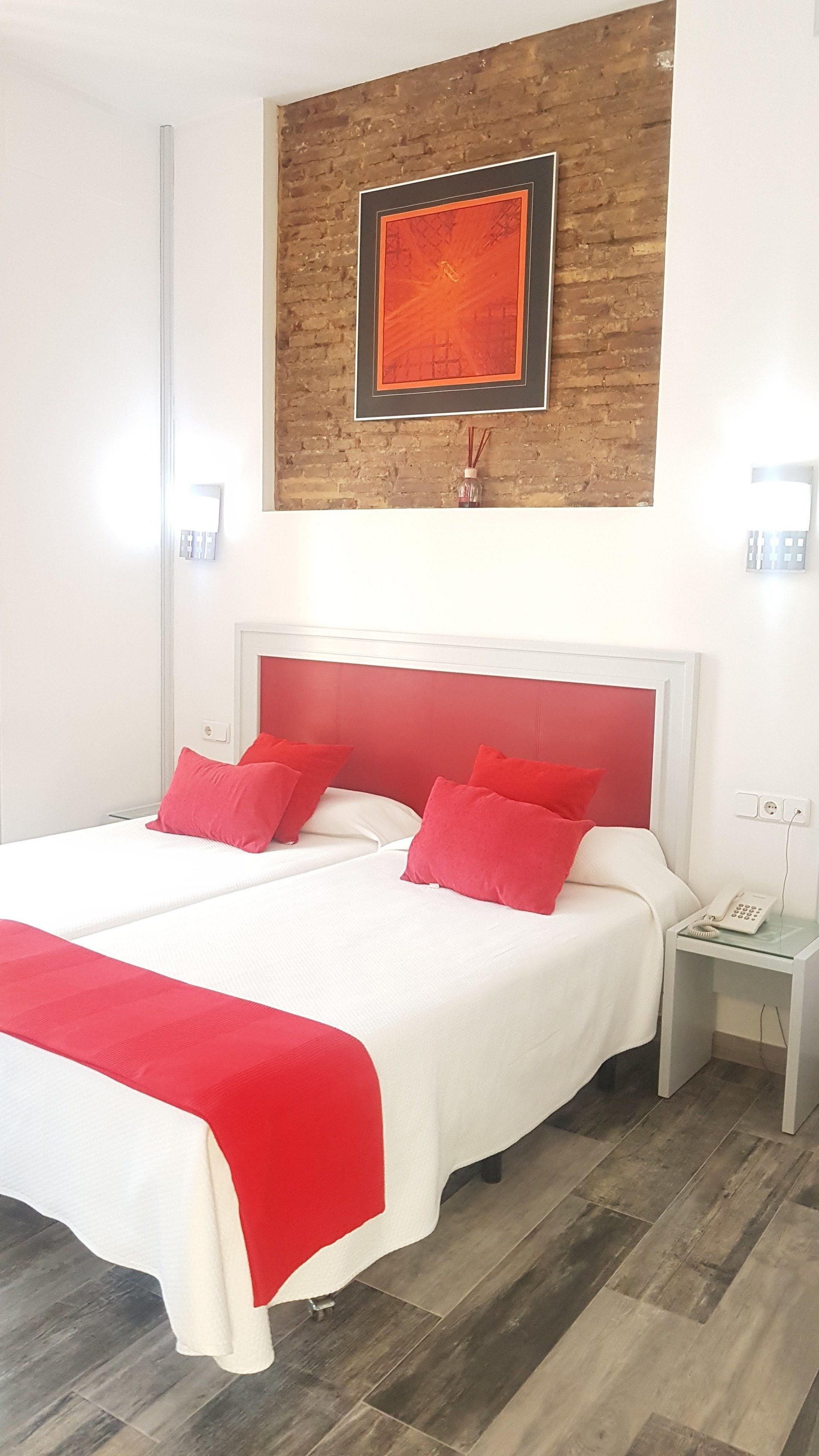 Habitació d'hotel amb un llit gran, almoinades vermelles, un panell de capçal blanc, una paret decorativa de fusta i una taula de nit amb un telèfon.