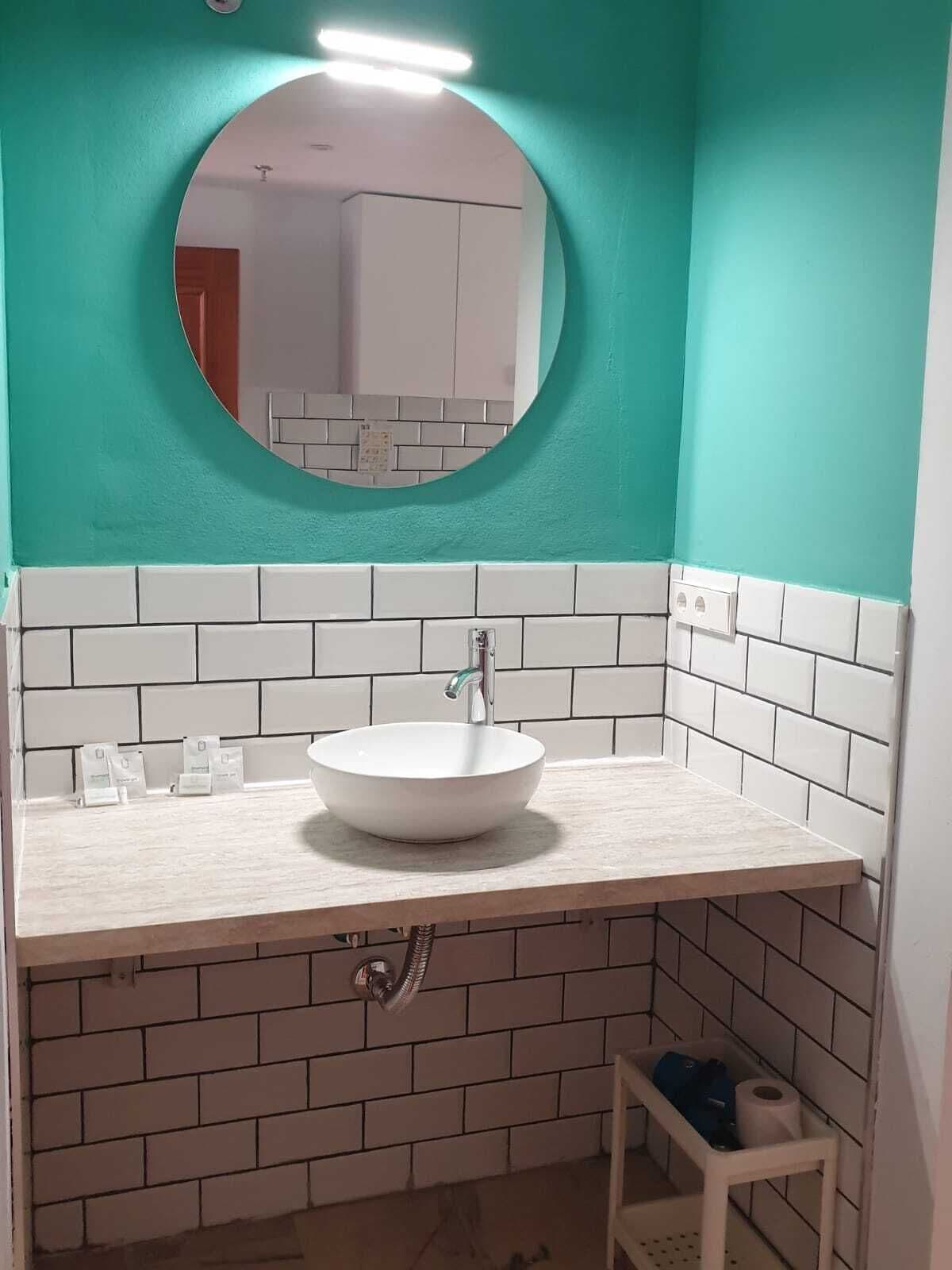 Een badkamer met een witte wastafel, een ronde spiegel en een witte betegelde spatwand.