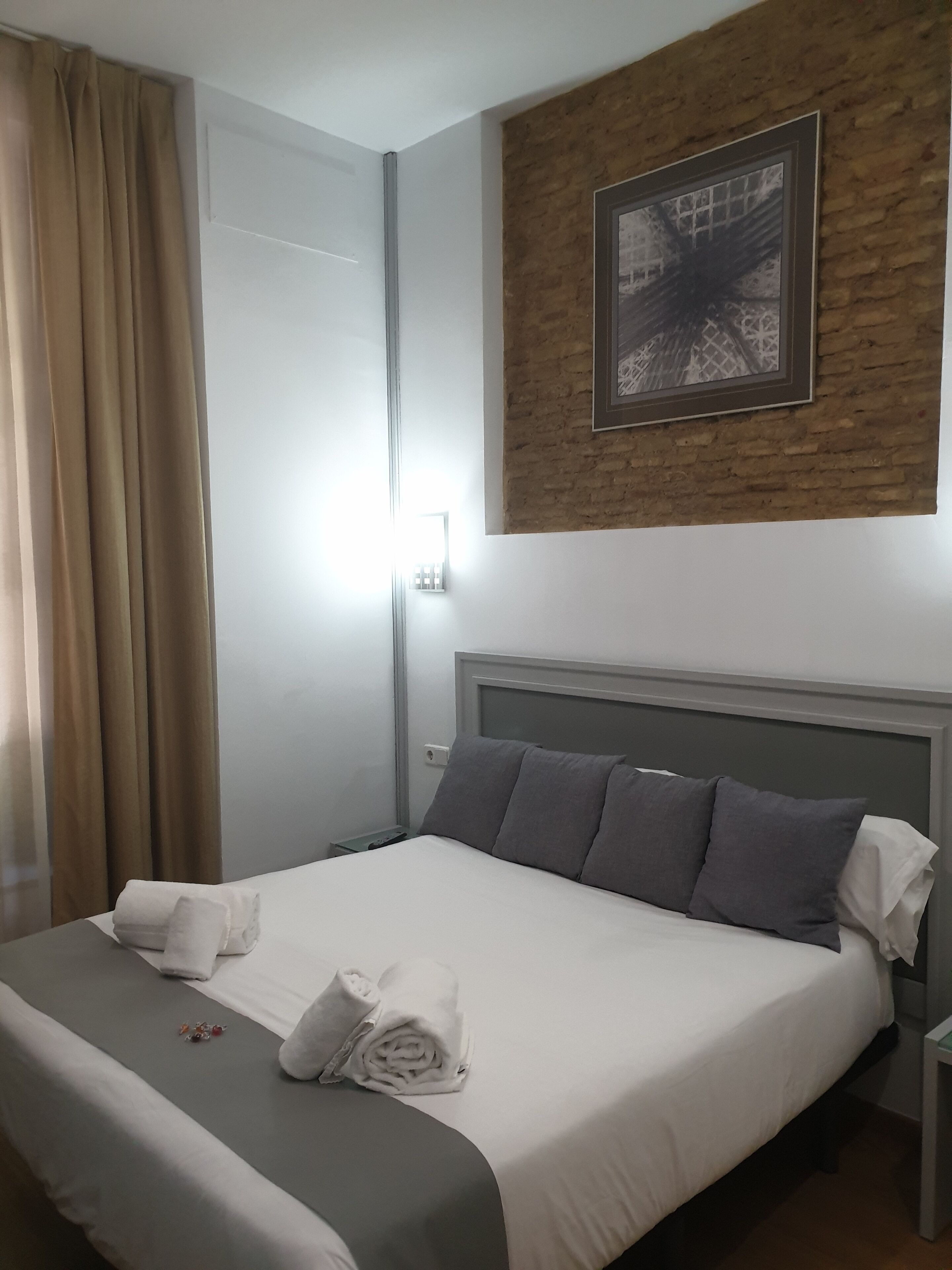 A hotel room with a neatly made bed, a headboard, a framed picture on the wall, and a window with curtains.