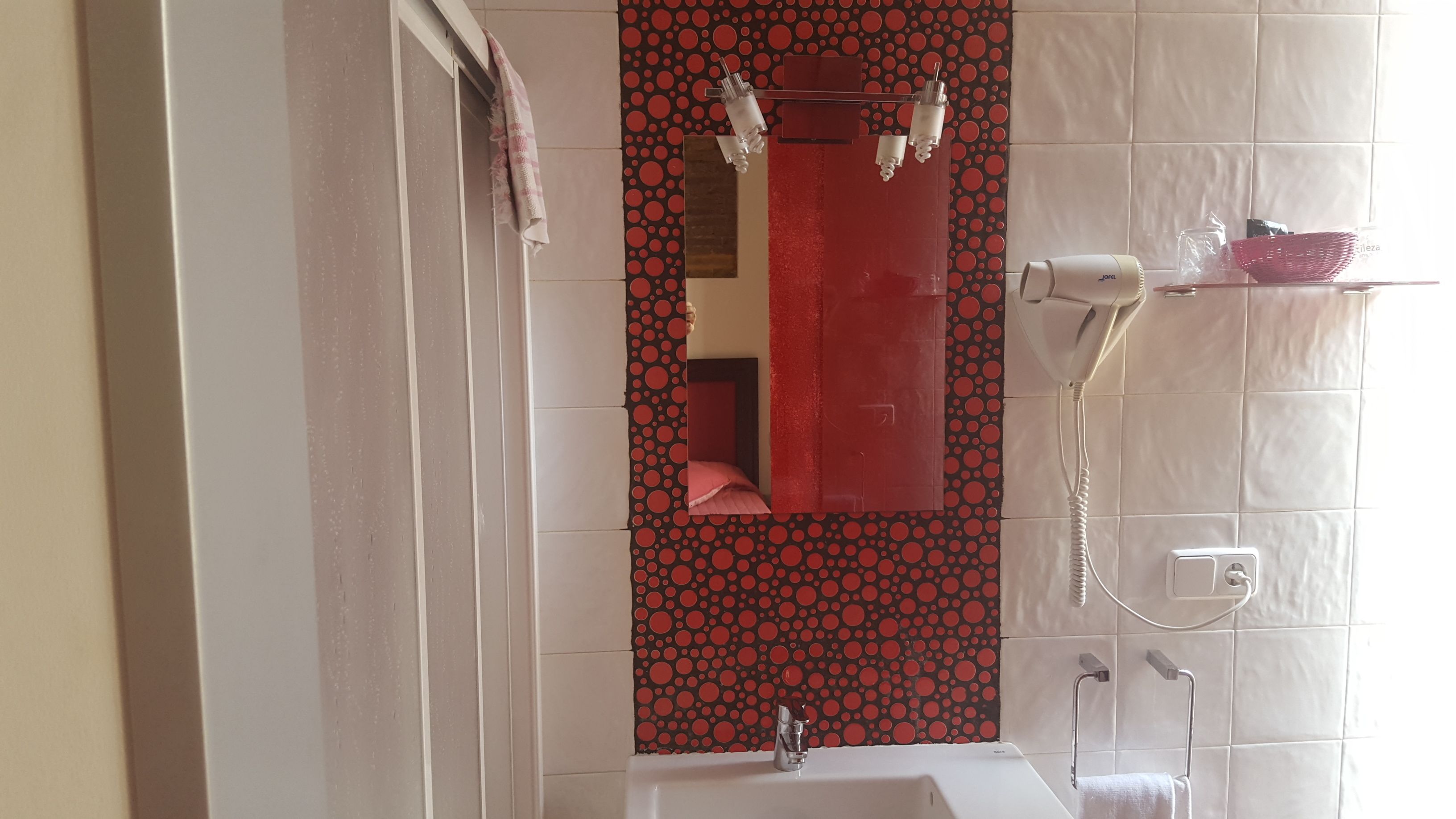 Ein Badezimmer mit einem weißen Waschbecken, einem roten Spiegel und einer Duschkabine.