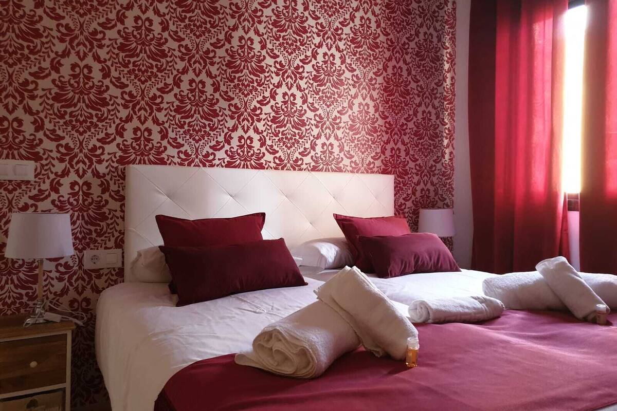 A hotel room with a large bed, red and white patterned wallpaper, and red curtains.