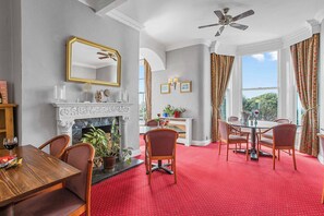 A dining area with a red carpet, a fireplace, and a dining table with chairs. - Royal Beacon Hotel (Exmouth)