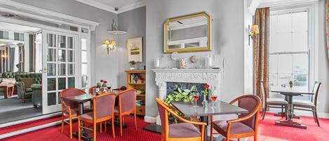A dining area with a red carpet, wooden chairs, a white table, and a fireplace.