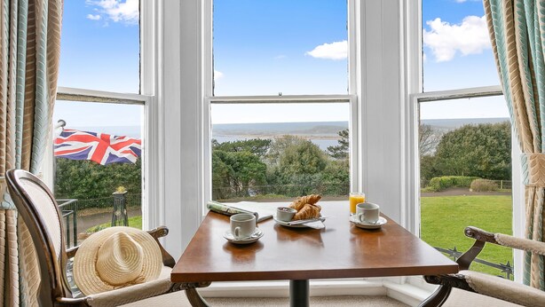 A breakfast table with croissants, a cup, and a saucer, set against a view of a grassy landscape and a flag. - Royal Beacon Hotel (Exmouth)