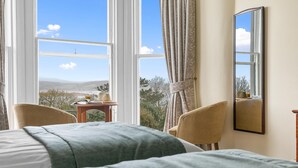 A hotel room with a large window, a bed, two chairs, a small table, and a mirror on the wall. - Royal Beacon Hotel (Exmouth)