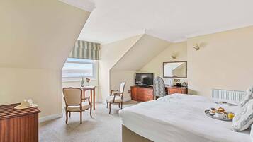 A bedroom with a large bed, a desk, a chair, a television, and a breakfast tray.