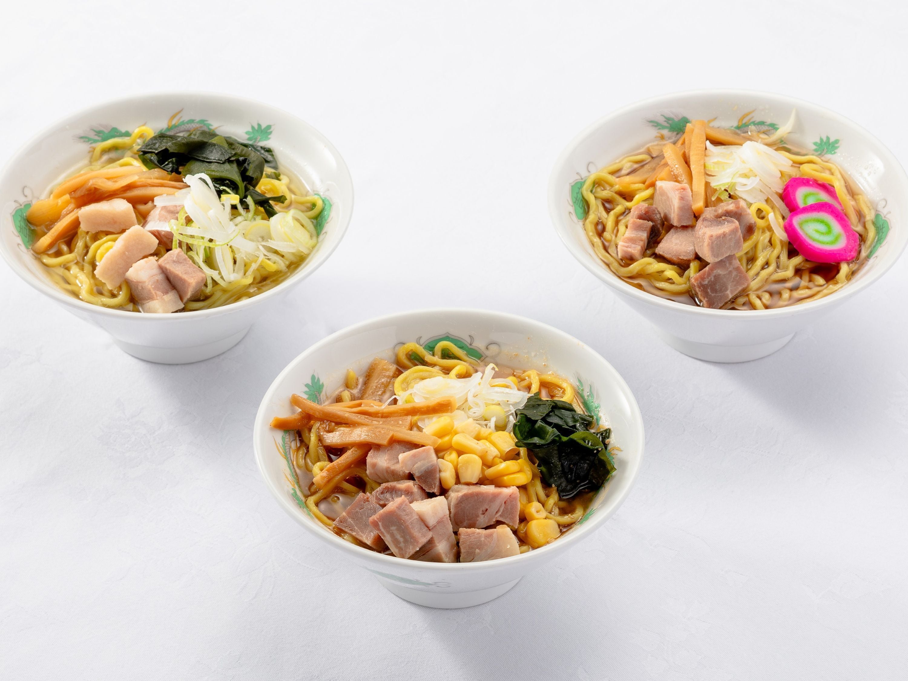 Three bowls of ramen with various toppings.