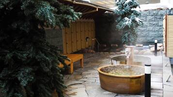 A stone-floored spa area with a wooden bench, a hot spring, and a pine tree.