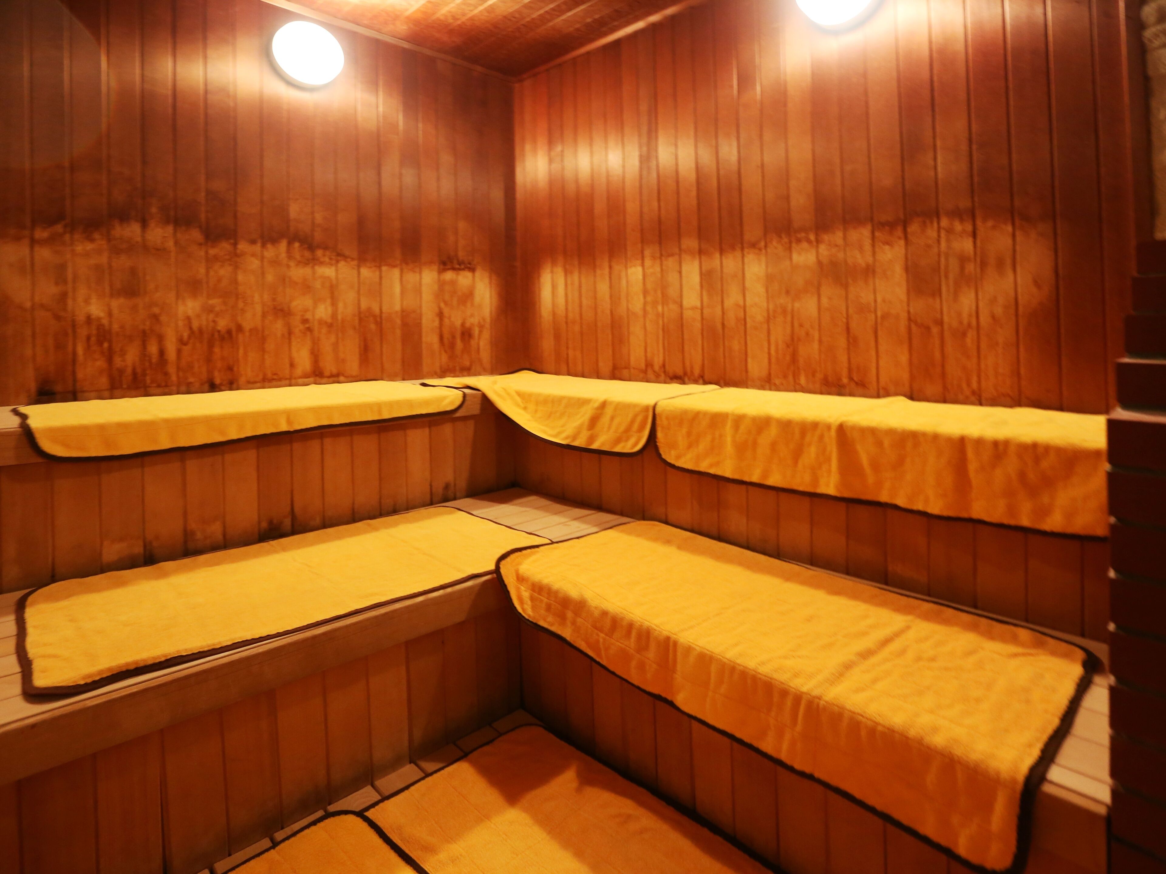 A sauna with wooden walls and benches, each with a yellow towel.