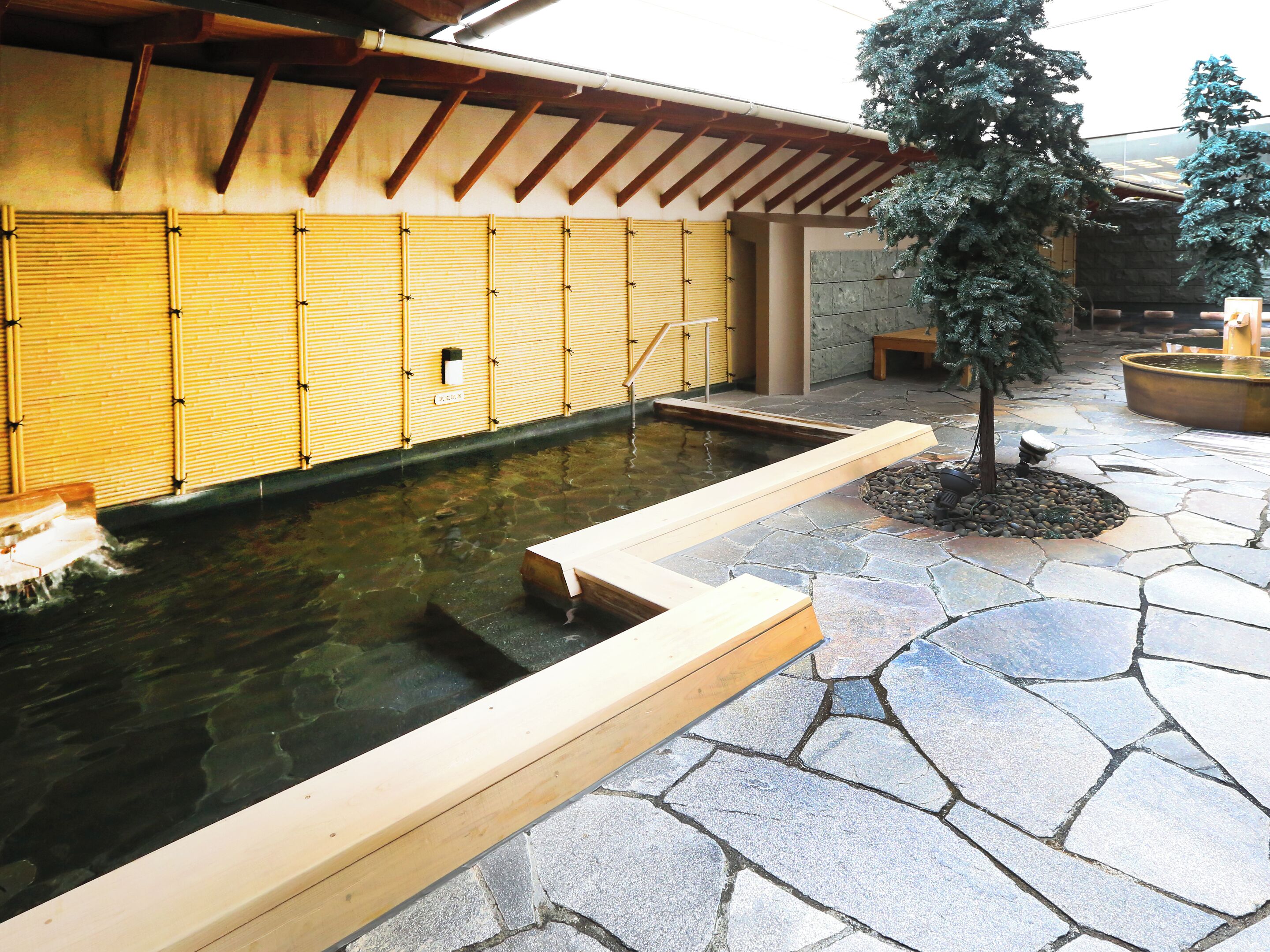 Un bâtiment de style japonais traditionnel, doté d’une cour dallée de pierres, d’un petit étang et d’une terrasse en bois.