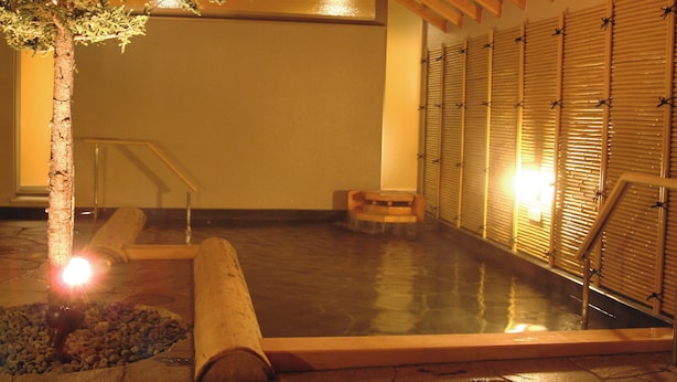 A spa area with a hot tub, wooden benches, and a tree with lights. - APA Hotel & Resort Sapporo (Sapporo)