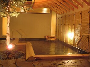A spa area with a hot tub, wooden benches, and a tree with lights. - APA Hotel & Resort Sapporo (Sapporo)