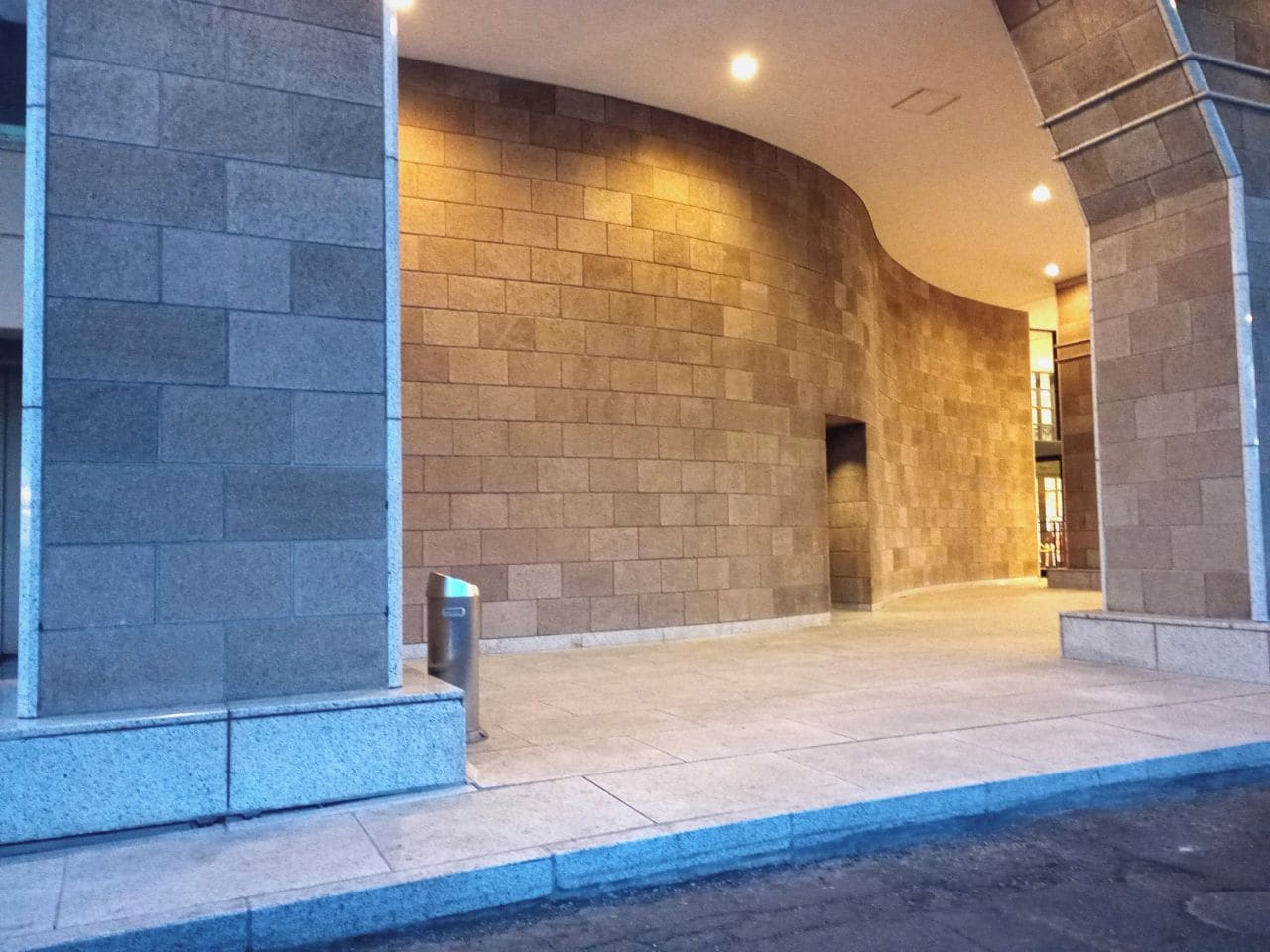 A building entrance with a curved wall and a trash bin.