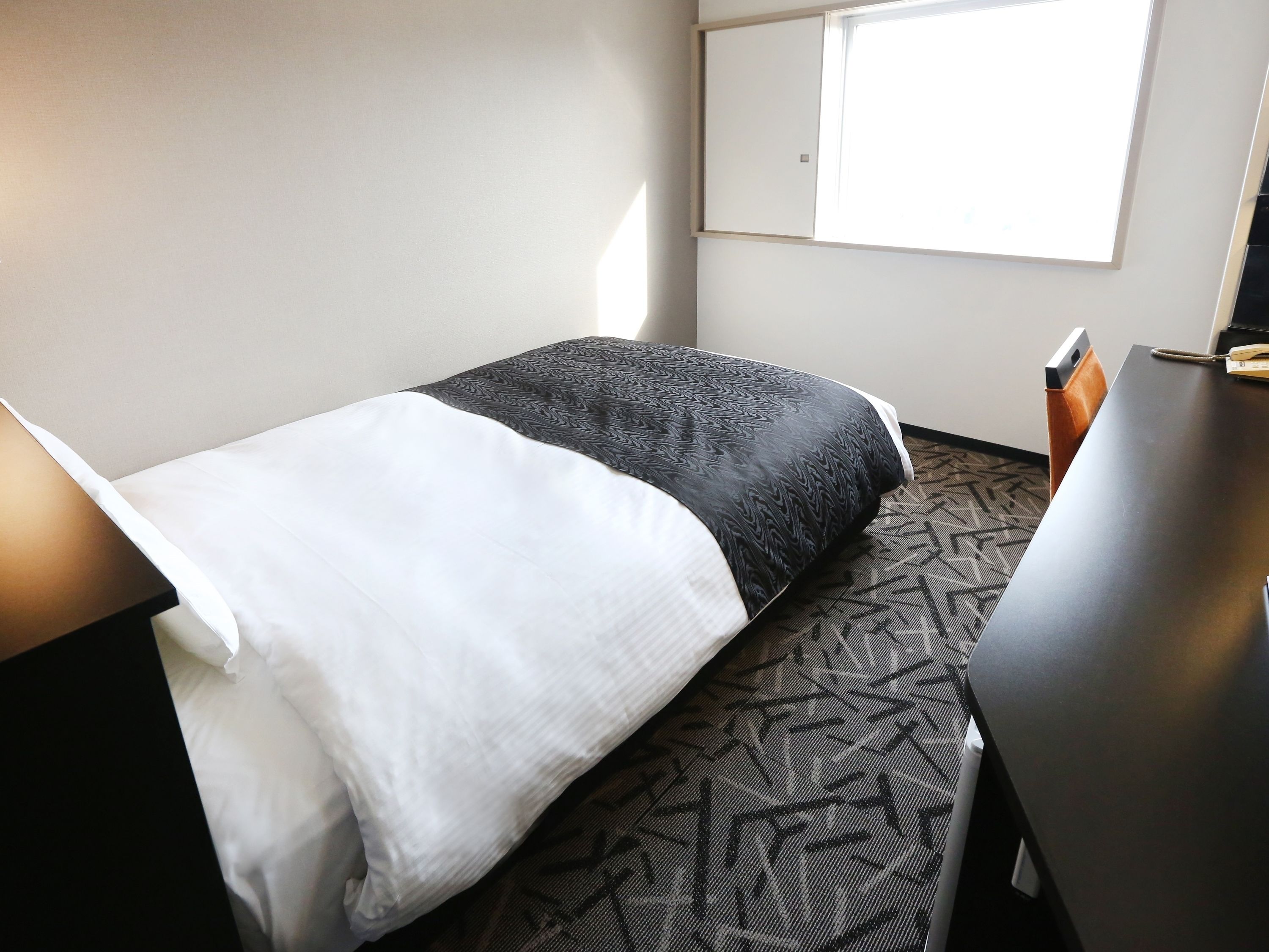 A hotel room with a bed, a desk, and a window.