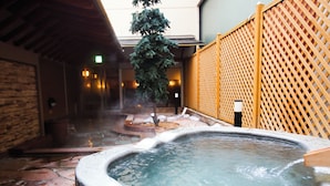 A hot spring area with a stone bath, wooden fence, and a tree. - APA Hotel & Resort Sapporo (Sapporo)