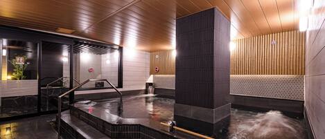 Un spa moderno con techo de madera, bañera de hidromasaje y una pequeña cascada.