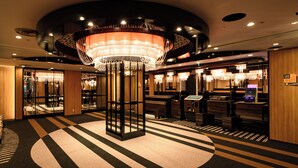 Un moderno vestíbulo de hotel con una araña central, quioscos de recepción y una alfombra estampada.