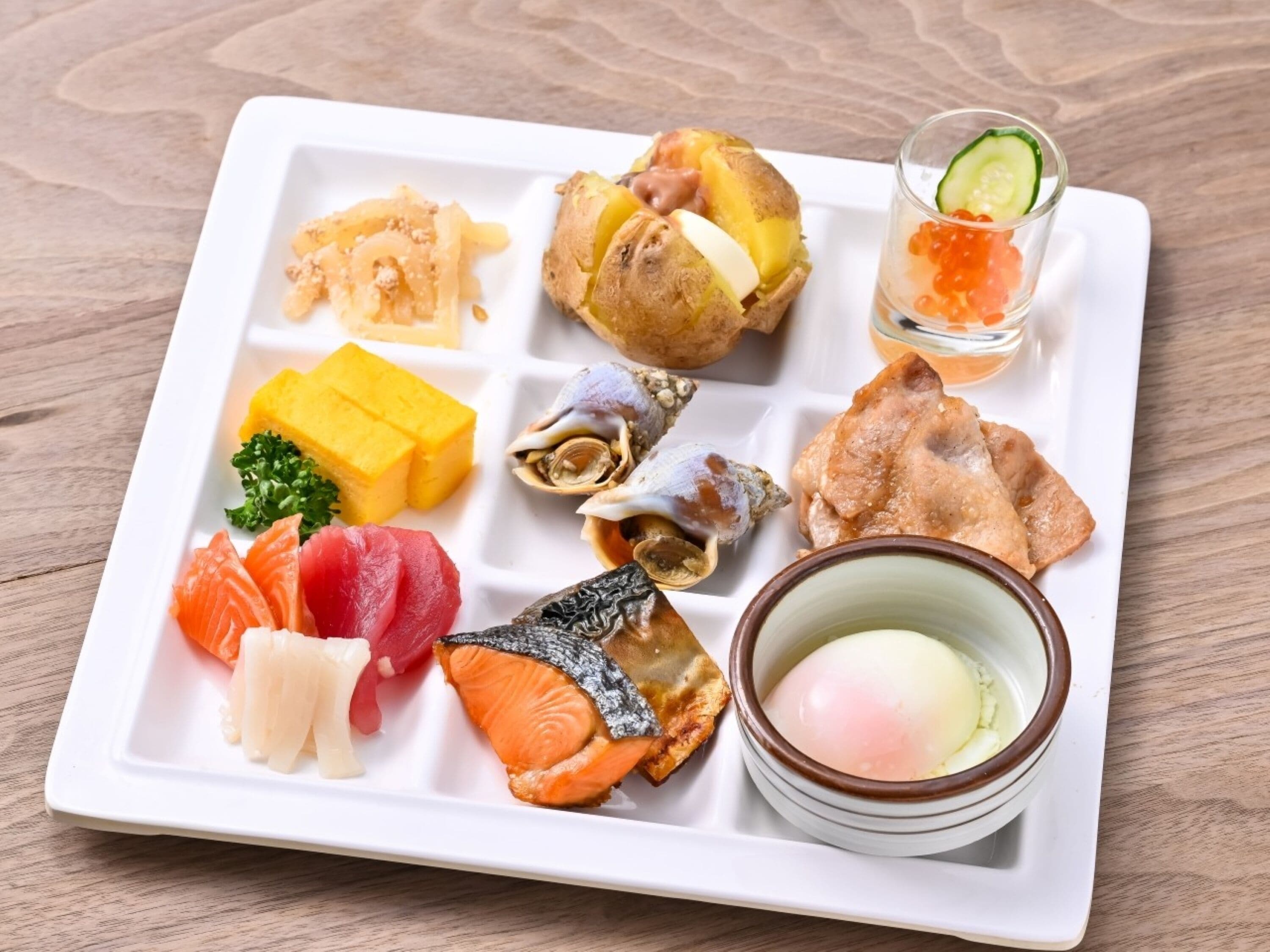 A white rectangular plate with various food items including sushi, sashimi, and a bowl of egg.