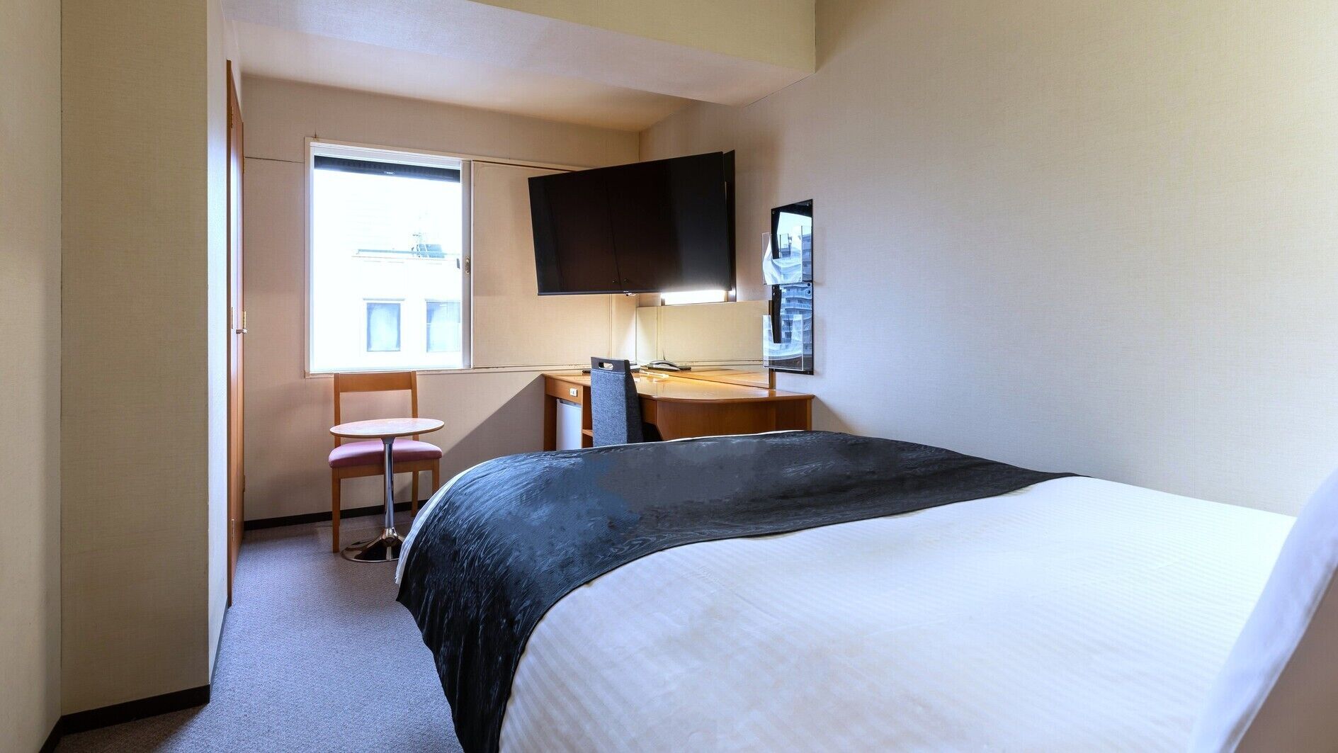 A hotel room with a bed, a desk, a chair, a TV, and a window.