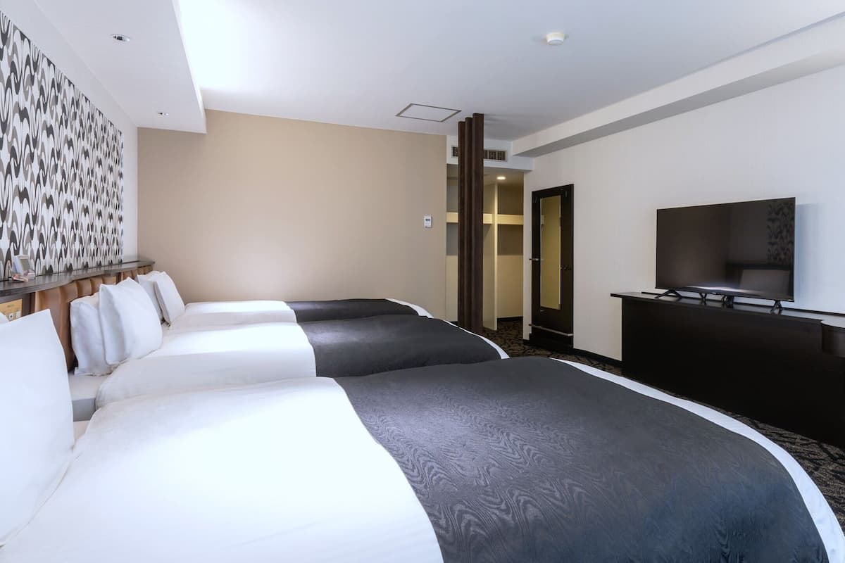 A hotel room with three beds, a TV, a desk, and a patterned wall.