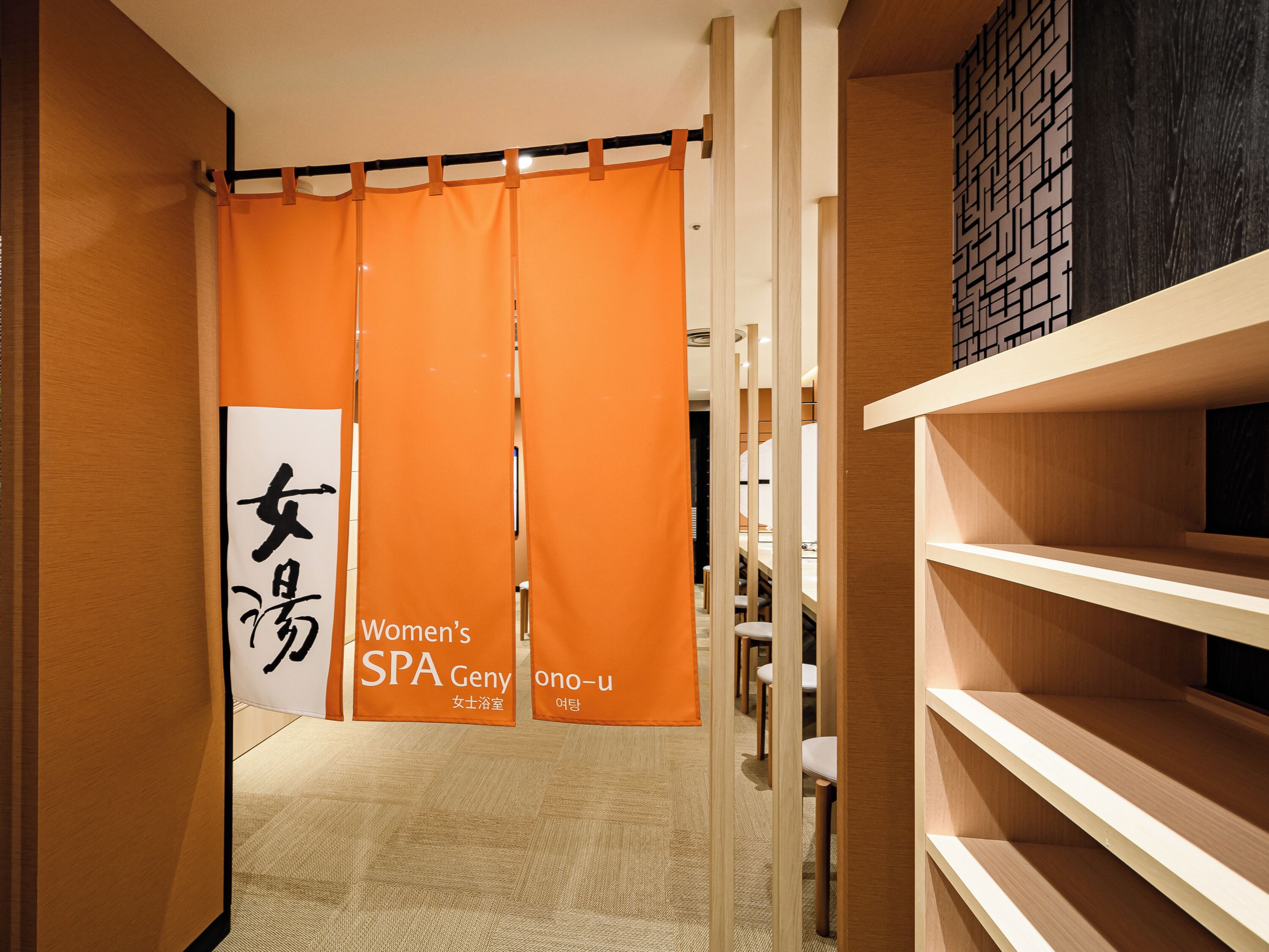A corridor with orange partitions, a sign for Women's SPA Geny, and a wooden wall with shelves.